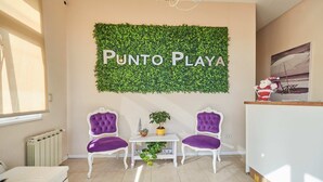 Una habitación con dos sillones morados tapizados, una mesita blanca y un letrero verde fijado a la pared que dice "PUNTO PLAYA".