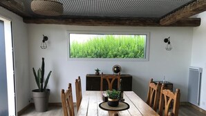 Zona pranzo con tavolo in legno, sedie, una pianta in vaso e una finestra vista su spazi verdi.