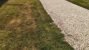 Una casa moderna con un'ampia vetrata, un vialetto sterrato e un prato ben curato.