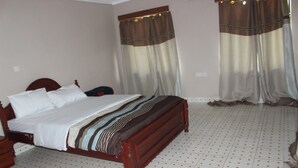 A bedroom with a wooden bed, white bedding, curtains, and a tiled floor. - Namelok Retreat Centre (Nyahururu)