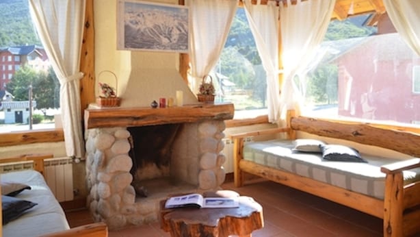 Una habitación acogedora con chimenea de piedra, un banco de madera y vistas a las montañas.