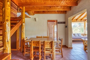 Un comedor de madera con una mesa grande y sillas, una escalera y vistas al exterior.