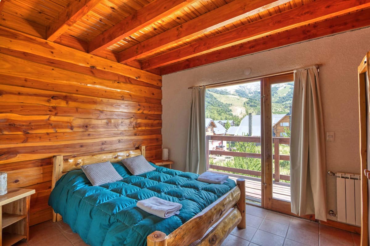 A wooden cabin bedroom with a bed, a nightstand, and a window with curtains.
