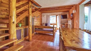 Interior de una cabaña de madera con una larga mesa de comedor, una escalera y un televisor.