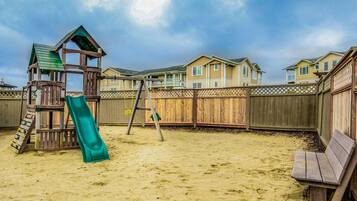Backyard features a play structure with a slide and climbing ladder, surrounded by a fence and a bench.