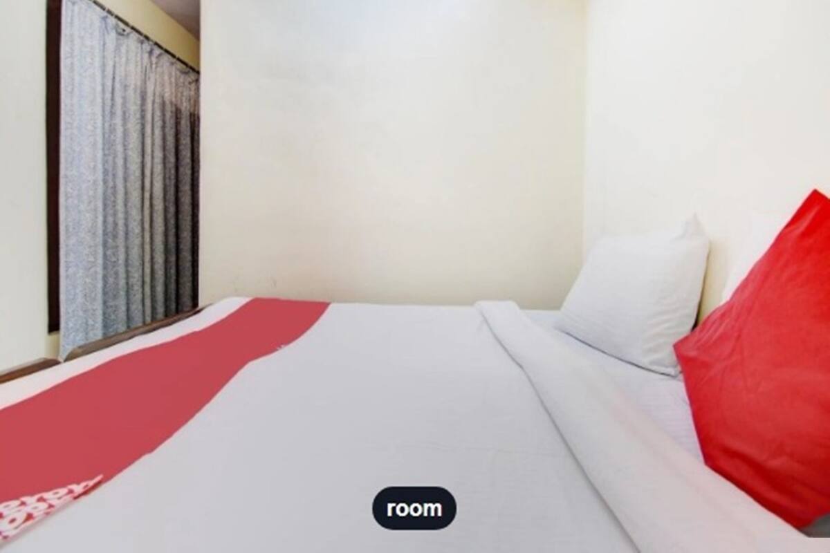 Una habitación con una cama, una colcha roja y blanca, y un ventanal con cortinas.