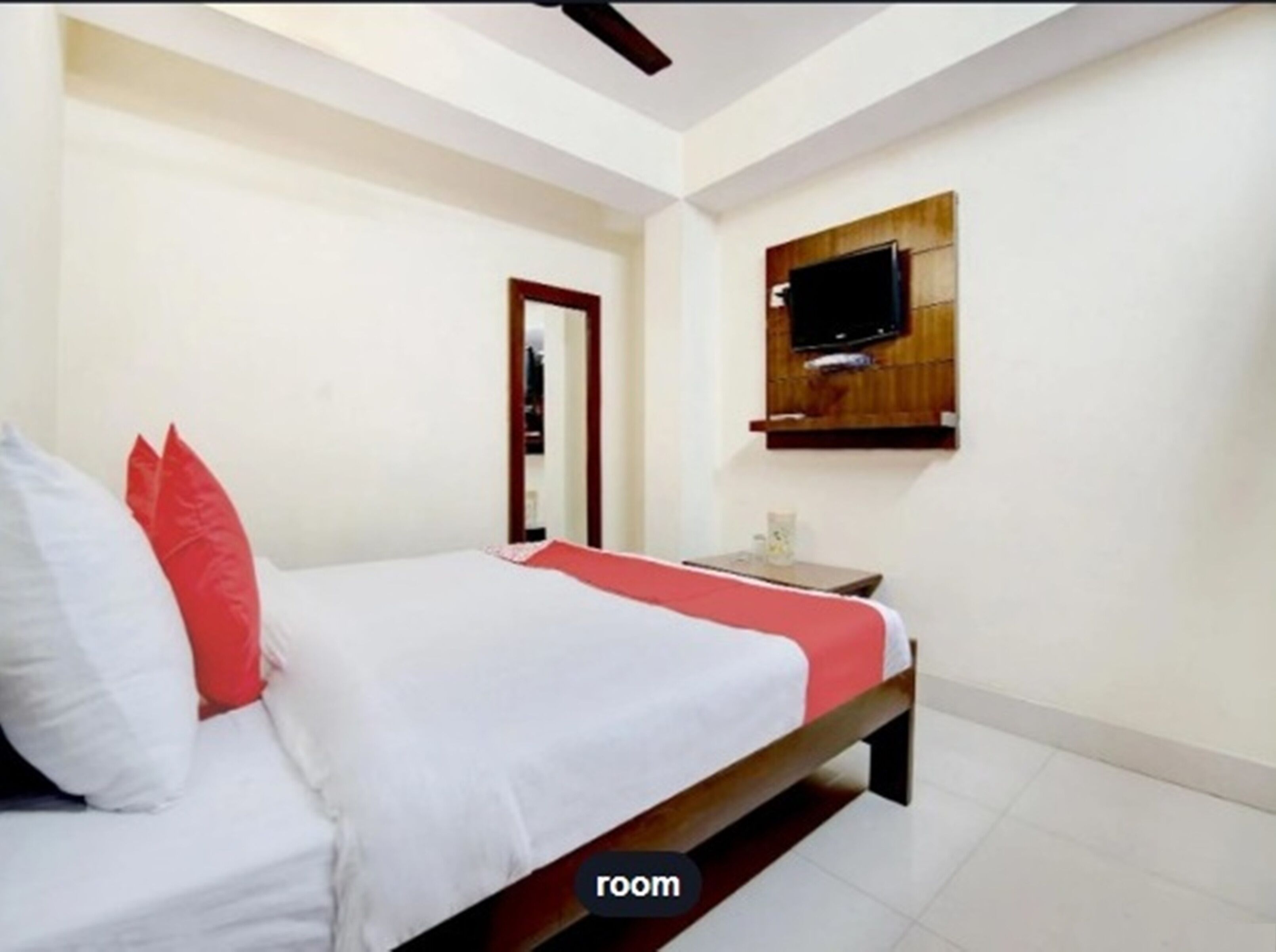 A hotel room with a bed, a television mounted on the wall, and a small table with a vase.