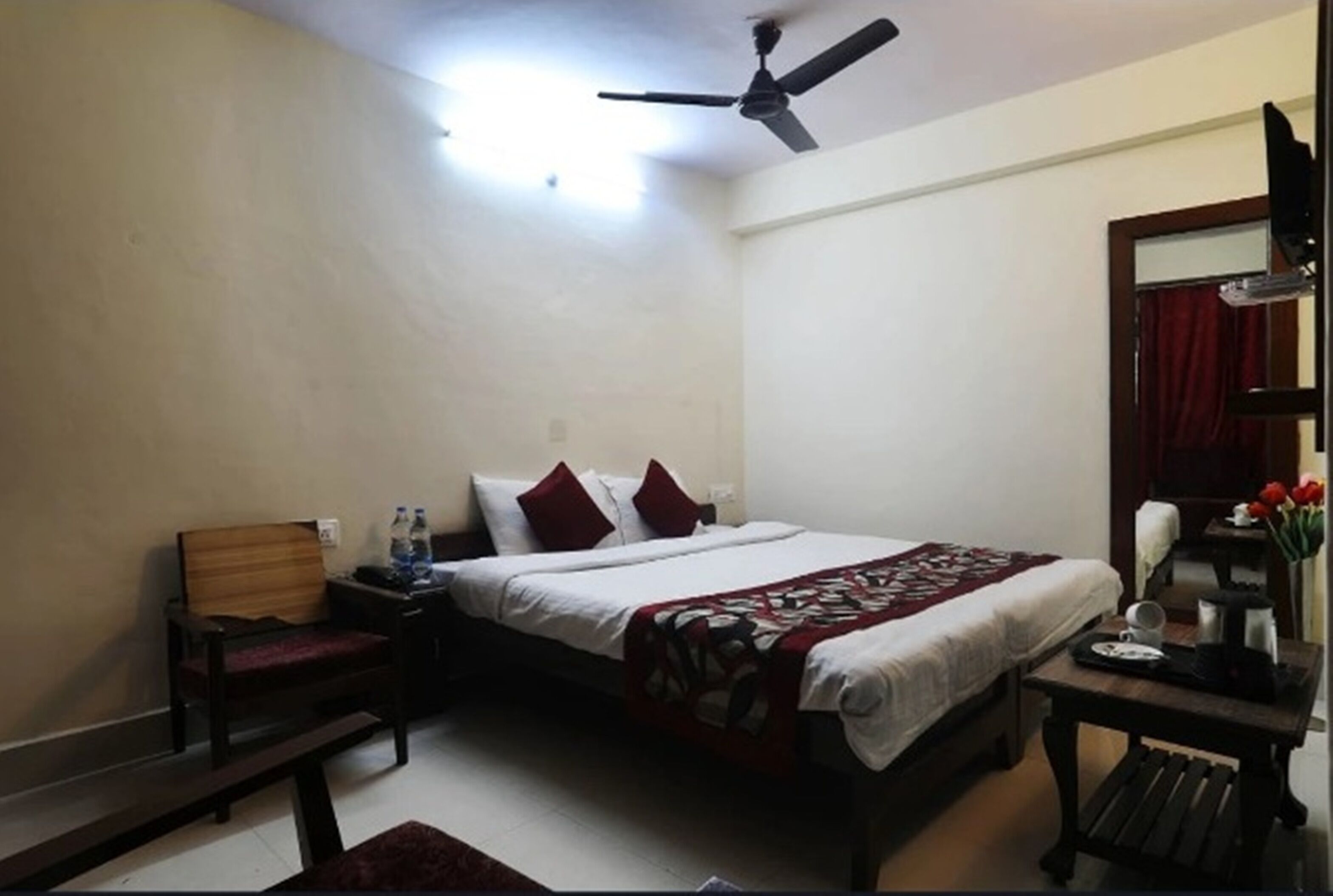 Quarto com cama, mesa de cabeceira, cadeira, mesa com um vaso de flores e ventilador de teto.