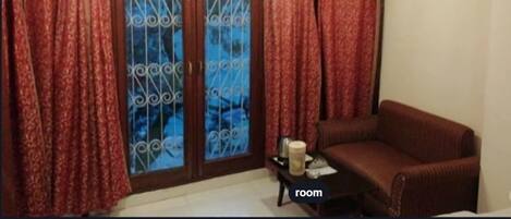 A room with a brown sofa, a small table with a candle, and a window with decorative iron bars and red curtains.