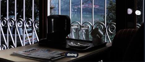 A dining area with a window view of a red train, a coffee maker, and a newspaper on the table.