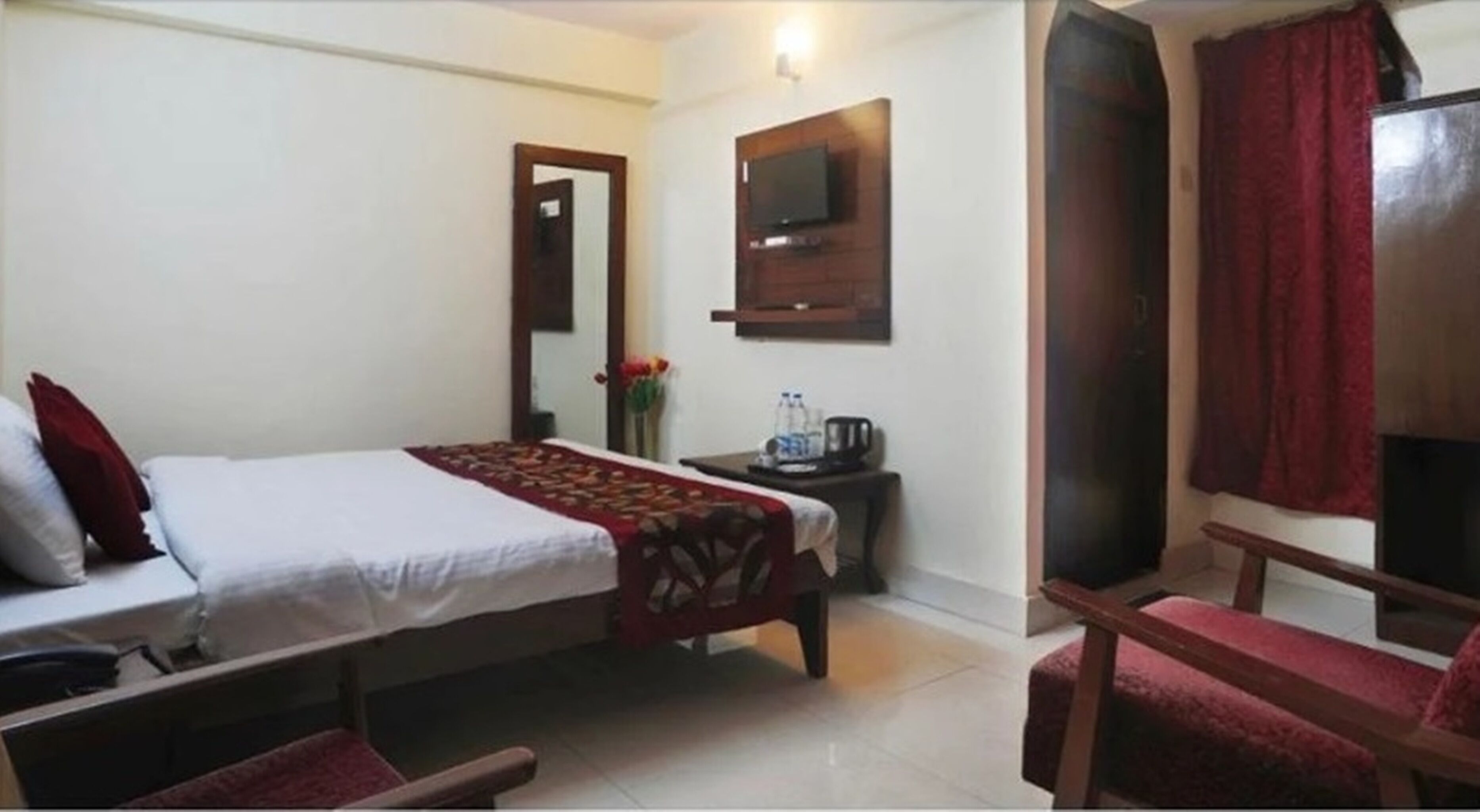 Habitación de hotel con cama, una mesita con hervidor, televisor montado en la pared y una silla.