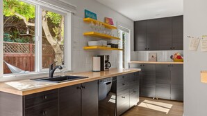 Une cuisine moderne avec des meubles de couleur sombre, un plan de travail en bois et un lave-vaisselle encastré. Des étagères au-dessus de l’évier servent à ranger les verres et les assiettes.