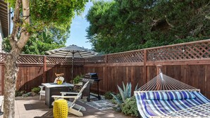 Un jardin avec une clôture en bois, un barbecue, un hamac et une table de patio.