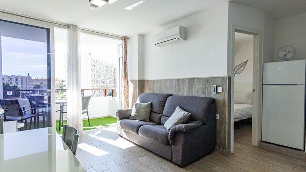 A modern apartment with a grey sofa, a dining table, and a kitchen area. - Starfish Friendly Holiday Home (Playa del Inglés)
