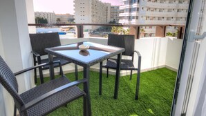 A balcony with a glass table and four wicker chairs, overlooking a cityscape with modern buildings. - Starfish Friendly Holiday Home (Playa del Inglés)