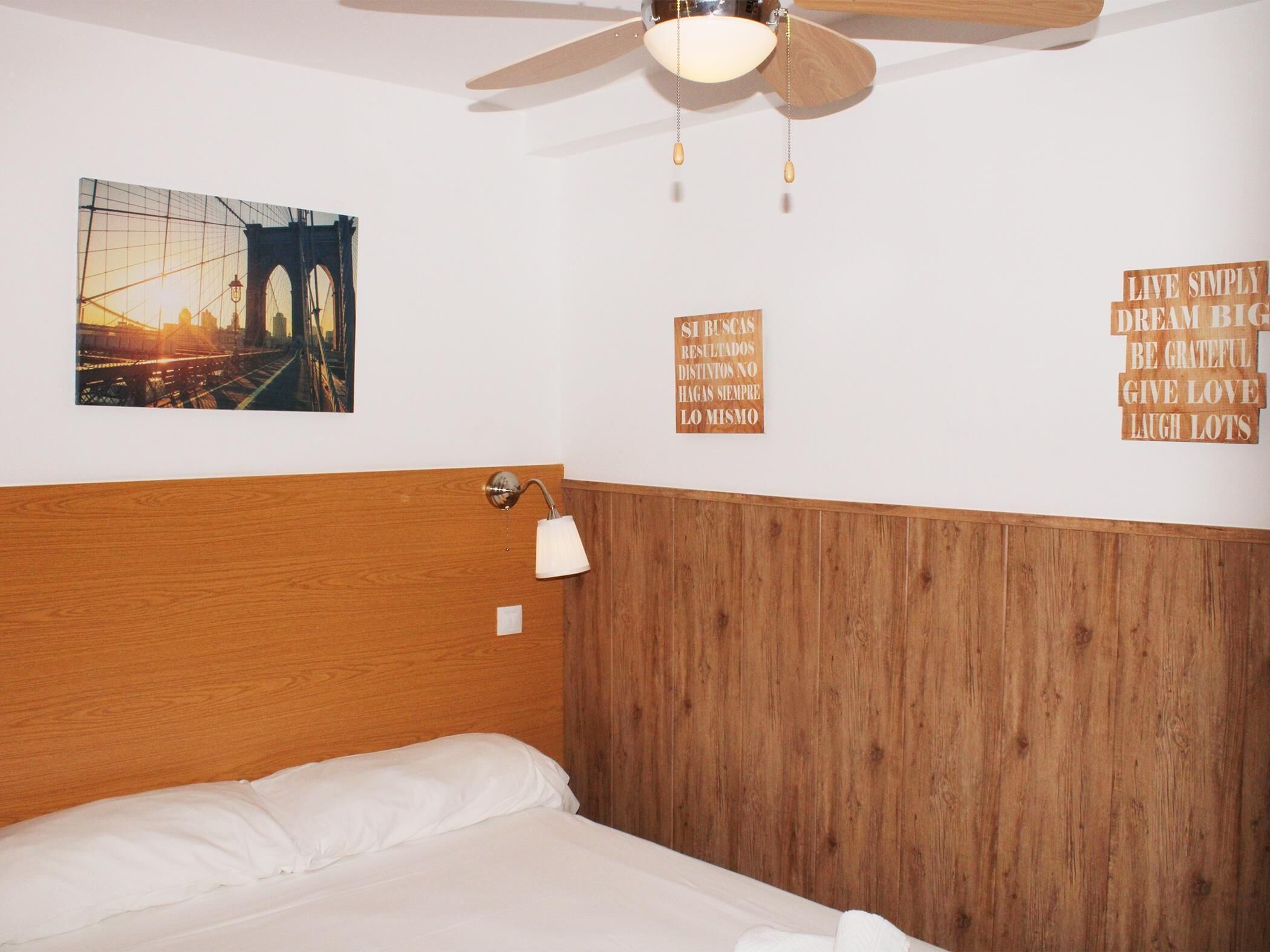 A hotel room with a wooden headboard, a bed with white linens, a wall-mounted lamp, and motivational posters.