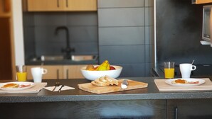 Eine moderne Küche mit Holzschränken, einer schwarzen Arbeitsplatte und einer Fruchtschale. Auf der Arbeitsplatte stehen zwei weiße Tassen und ein Glas Orangensaft.