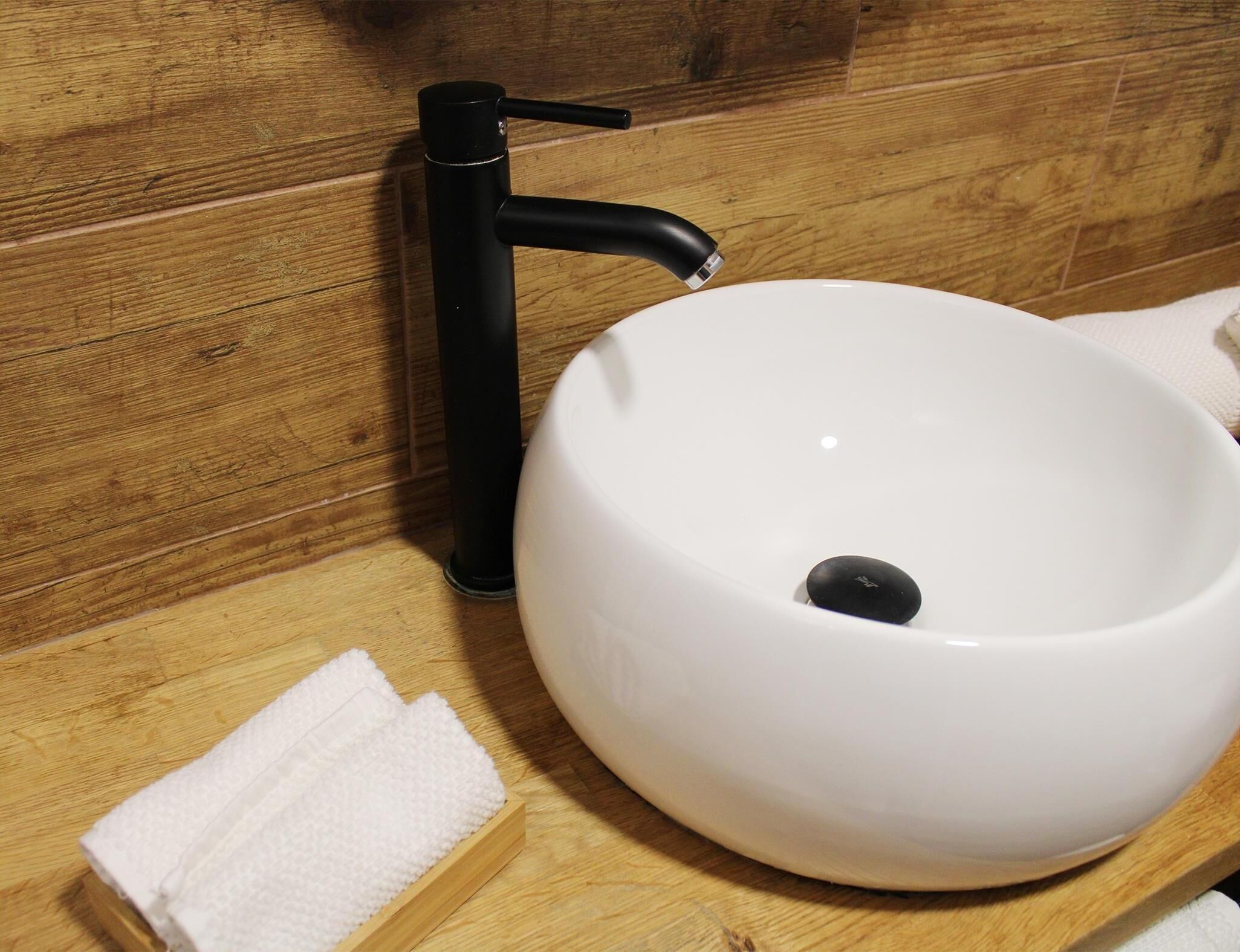 Un lavamanos blanco con un grifo negro, una toalla blanca y una superficie de madera.