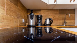 A modern kitchen with wooden cabinetry, a stainless steel coffee maker, and a kettle on a reflective countertop.