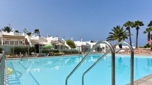 A swimming pool with clear blue water, surrounded by lounge chairs and umbrellas.