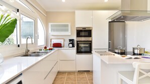 A modern kitchen with white cabinets, a built-in oven, a coffee maker, and a window with a plant.