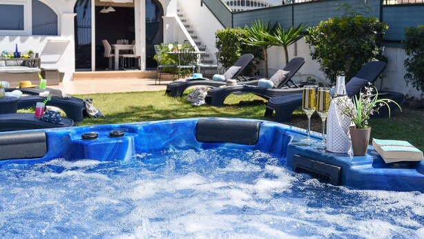 A swimming pool with lounge chairs and a hot tub, surrounded by a patio area with outdoor furniture and a staircase leading to a covered deck.
