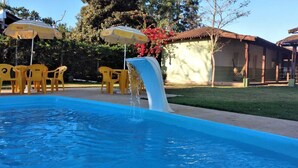 Una piscina con tobogán de agua, sillas amarillas y sombrillas.