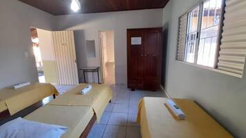 A hotel room with three single beds, a ceiling fan, a window with blinds, and a door.