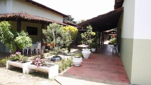 Un patio con plantas en macetas, un área de descanso techada y un edificio con techo de tejas.
