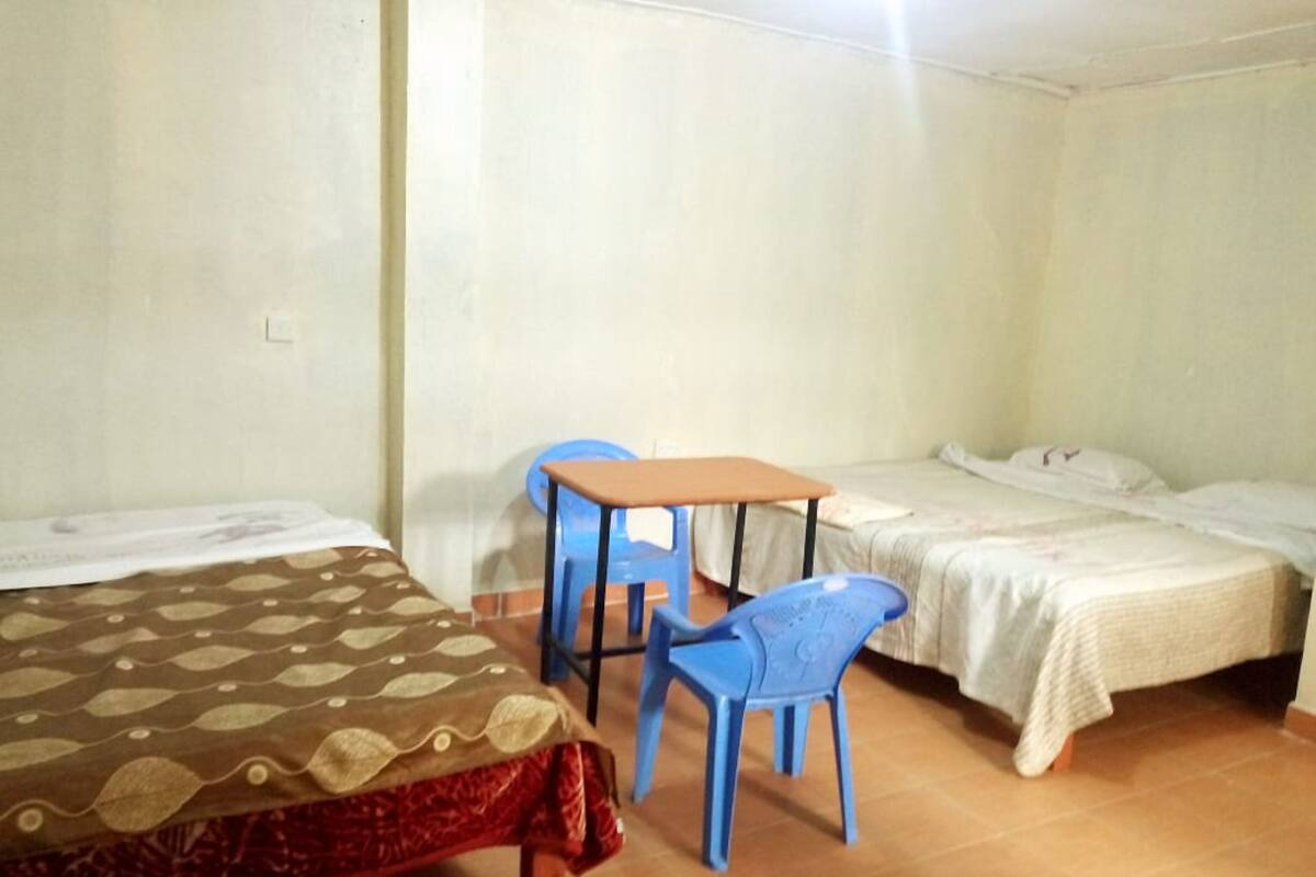 A room with two beds, a small table, and two blue chairs.