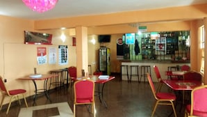 A restaurant with red chairs and tables, a bar area, and a refrigerator. - Rene Bistro Hotel (Nanyuki)