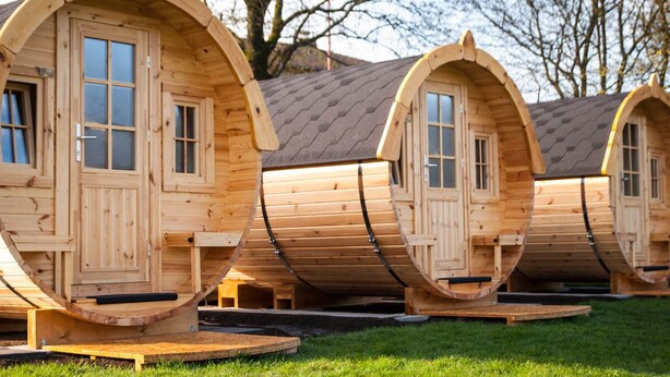 A row of wooden pod-style cabins with windows and doors, each elevated on a platform. - Harmony beim Holzschnitzer (Dreis-Brück)