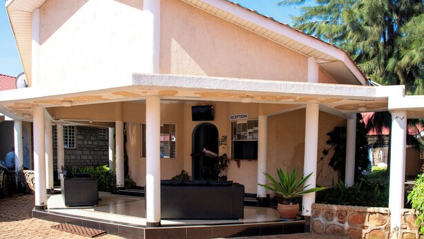 A building with a reception area, a TV mounted on the wall, and a covered outdoor seating area with potted plants. - Superbreak Hotel (Kitale)