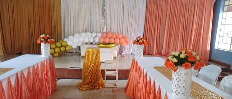 A decorated event space with a stage, white and gold table settings, and floral arrangements.