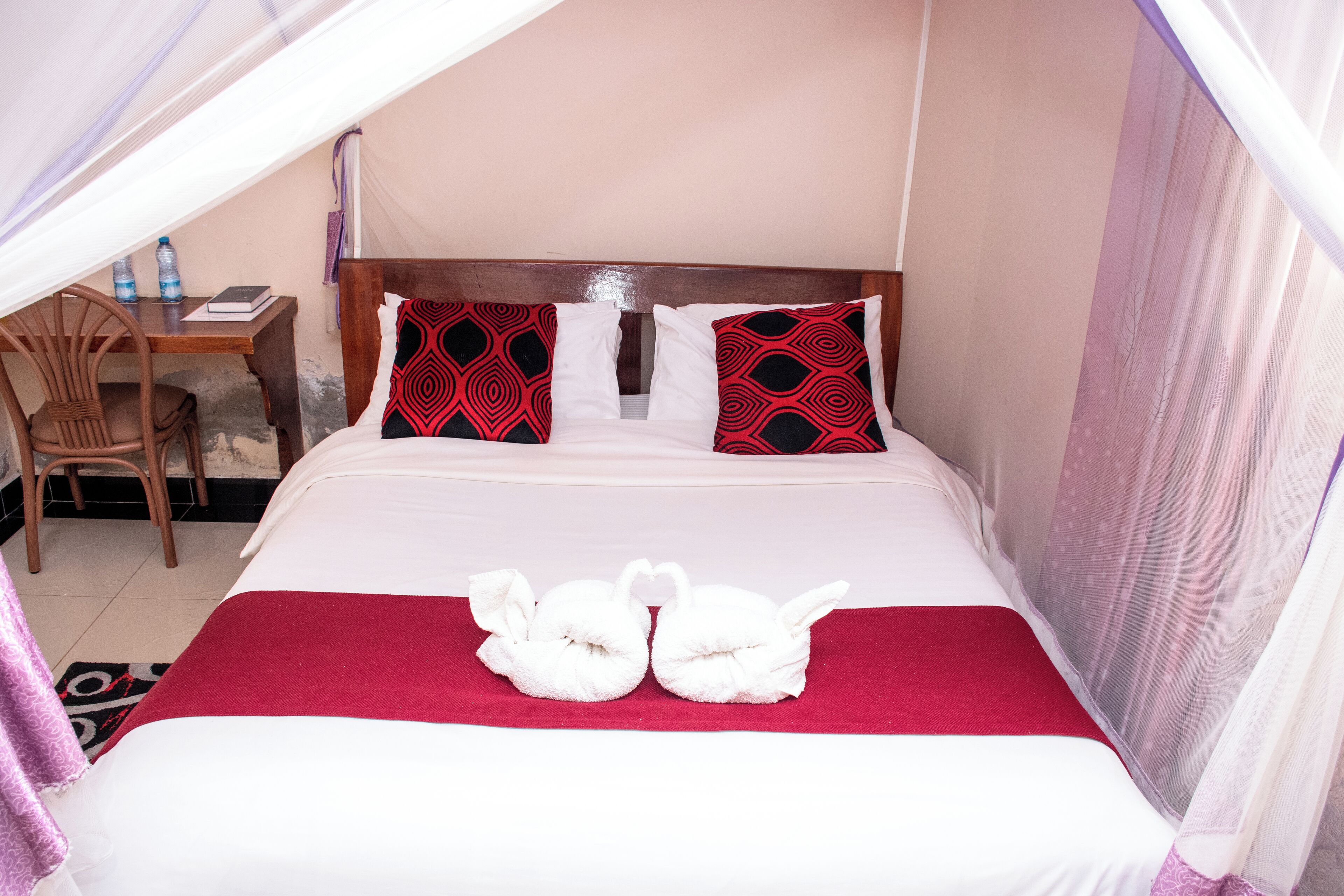 A neatly made bed with a red and white bedspread, two pillows with a red and black pattern, and two white towels shaped like swans.