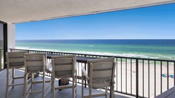 A balcony with three chairs facing the ocean.
