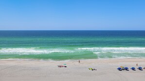A beach with clear skies, calm waters, and a few umbrellas and beach chairs.
