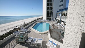 A pool area with lounge chairs and a view of the beach.