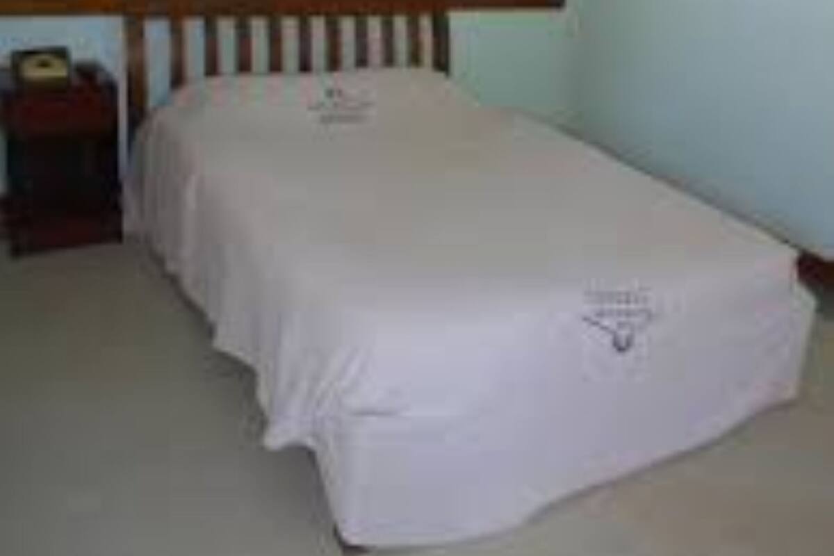 A single bed in a room with light blue walls, a wooden headboard, and a small bedside table with a lamp.