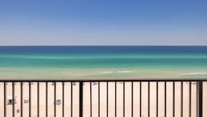 Vista de una playa desde un balcón con barandilla, cielo azul despejado y mar turquesa.