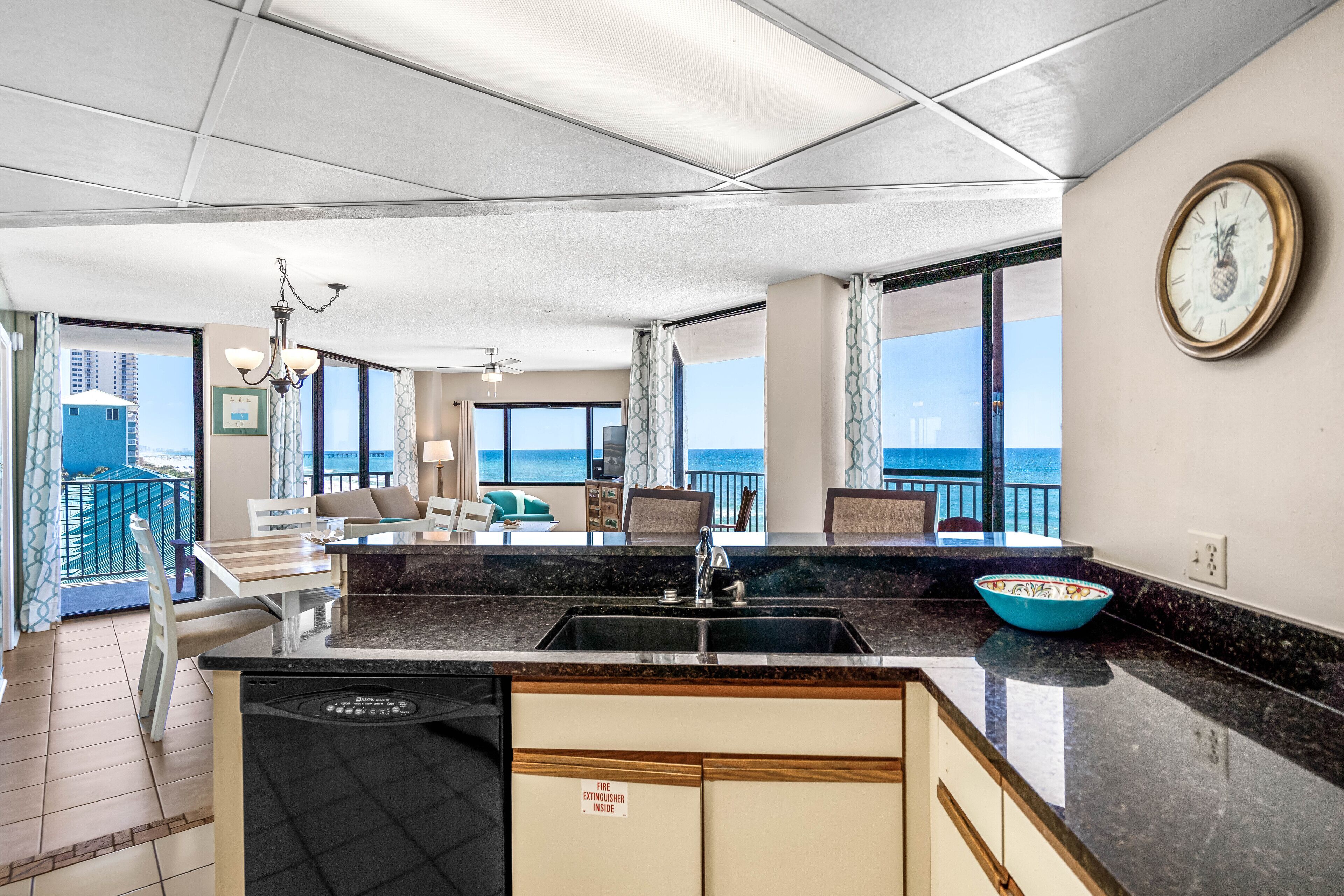 Een moderne keuken met een zwart aanrecht, een spoelbak en een blauwe kom. Er is een eethoek met een tafel en stoelen, en een balkon met uitzicht op de stad.