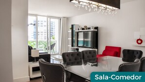 Un salon moderne avec une table à manger en verre, des chaises noires recouvertes de tissu, un canapé rouge, un téléviseur à écran plat et un lustre.