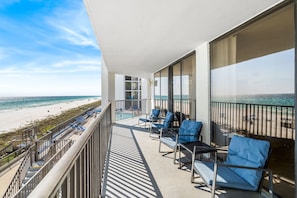 A balcony with blue cushioned chairs overlooking a beach.