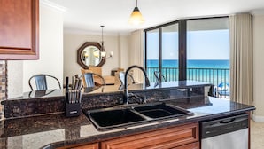 A kitchen with a view of the ocean, a sink, and a dining area with chairs.