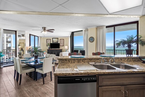A modern kitchen with granite countertops, a dishwasher, and a dining area with a table and chairs.