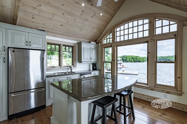 A kitchen with a large island, stainless steel appliances, and a view of a lake through large windows.