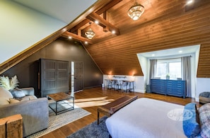 Un amplio dormitorio tipo loft con techo inclinado, una cama grande, un escritorio y una zona de estar.