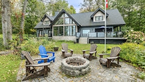 Una cabaña con un hogar de piedra, sillas Adirondack de madera y una terraza con vistas a un jardín.