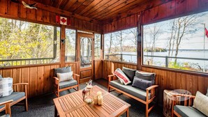 Una cabaña de madera con una zona de estar acogedora, grandes ventanas con vistas a un lago y una bandera canadiense.