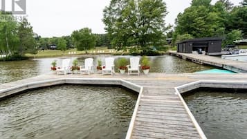 A wooden dock extending over a body of water, with white chairs and potted plants arranged on the dock.